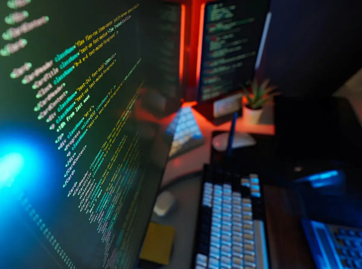 Dual monitors displaying code in a dark workspace, representing security monitoring for compliance
