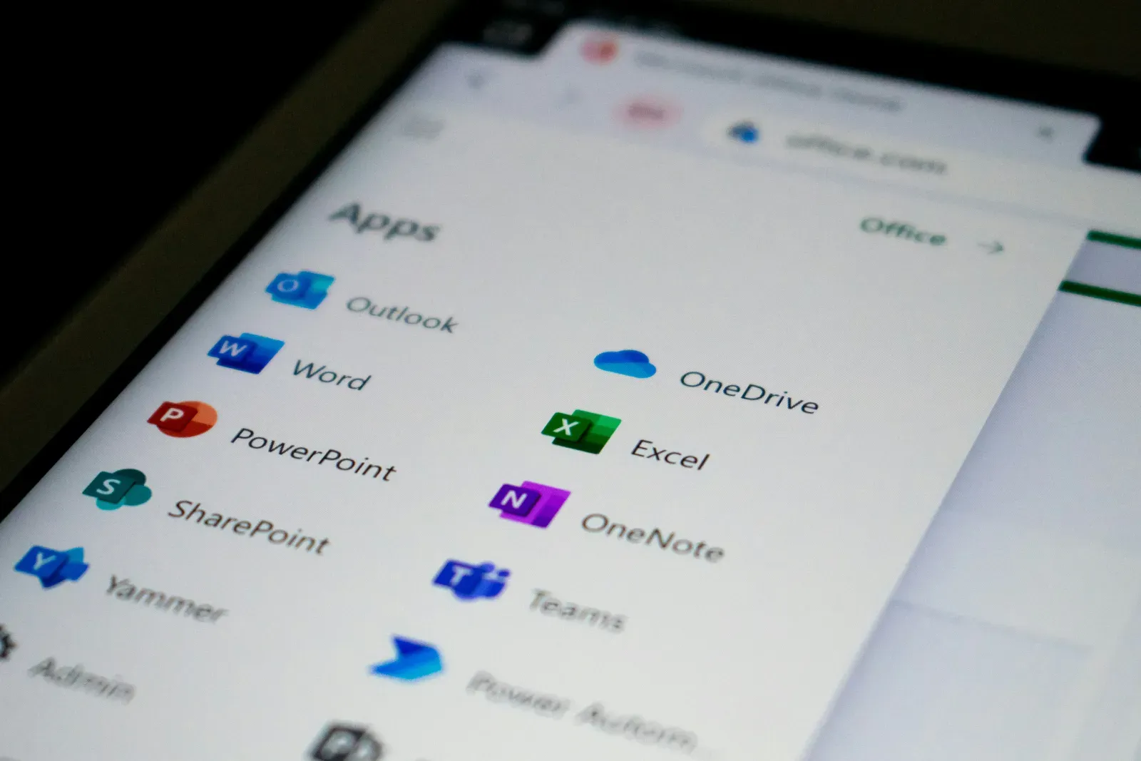 The Microsoft 365 app launcher open on a laptop screen, showing Outlook, Word, PowerPoint, SharePoint, OneDrive, Excel, OneNote, and Teams