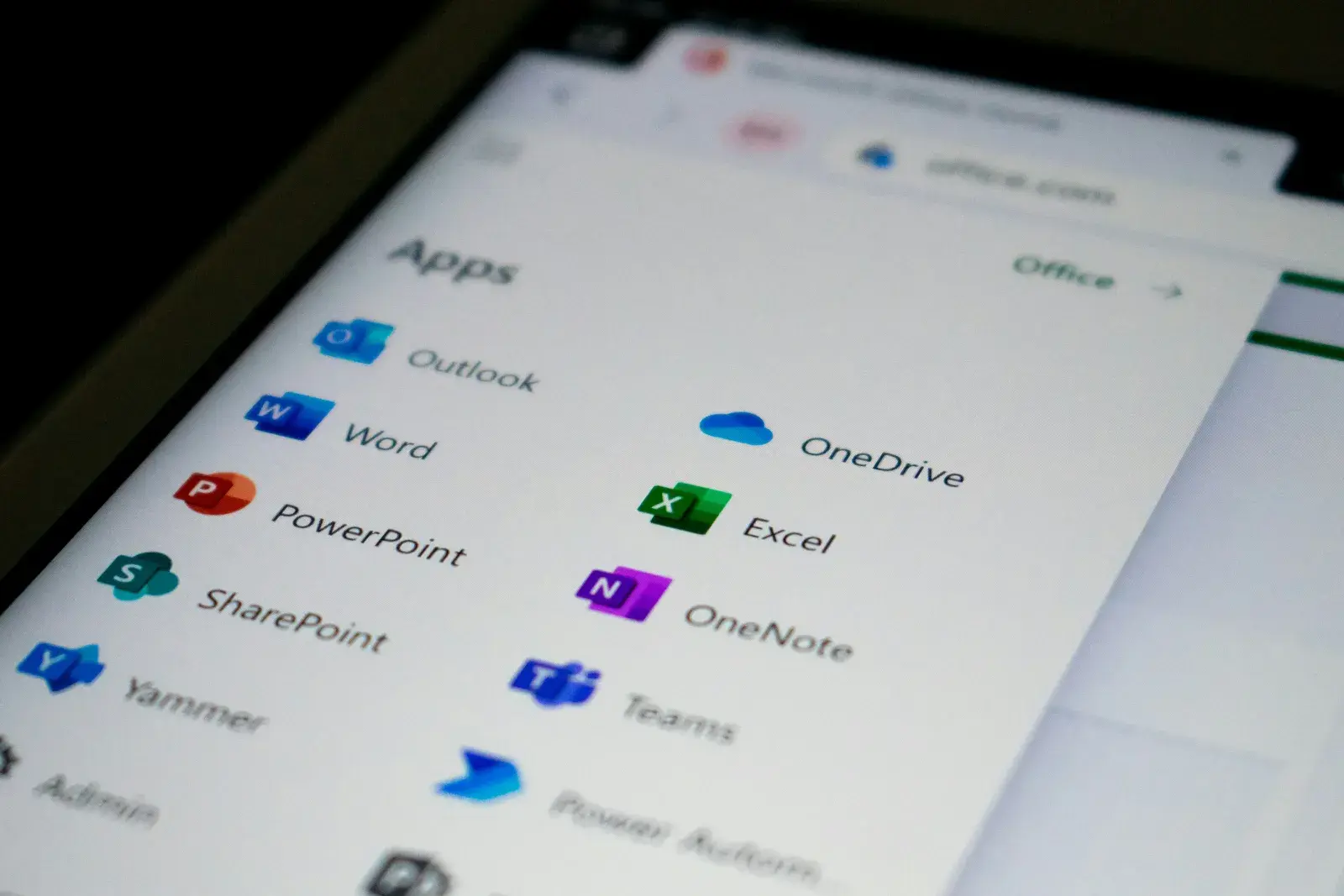 The Microsoft 365 app launcher open on a laptop screen, showing Outlook, Word, PowerPoint, SharePoint, OneDrive, Excel, OneNote, and Teams
