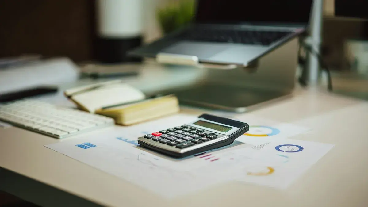 A calculator on printed charts beside a laptop and keyboard on an office desk
