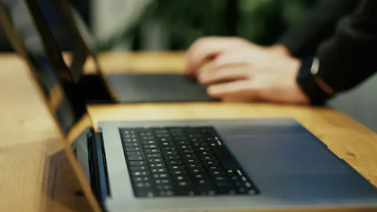 Two laptops open side by side on a wooden desk during a working session, illustrating an IT provider handover