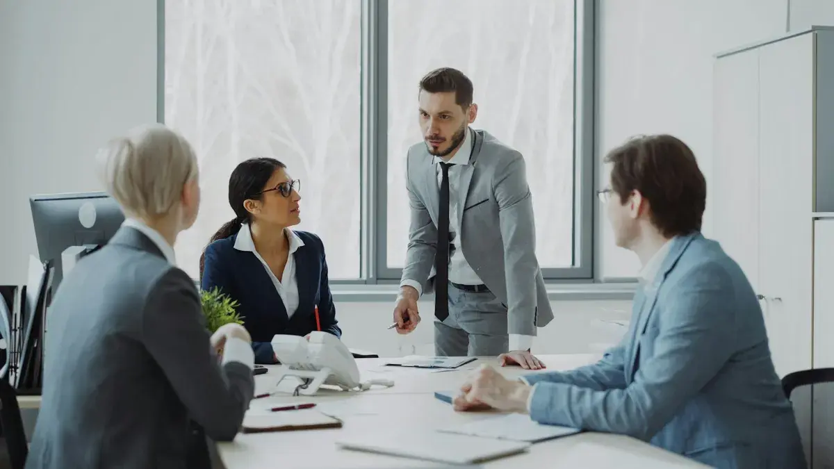 A man standing at a conference table leading a meeting with three colleagues