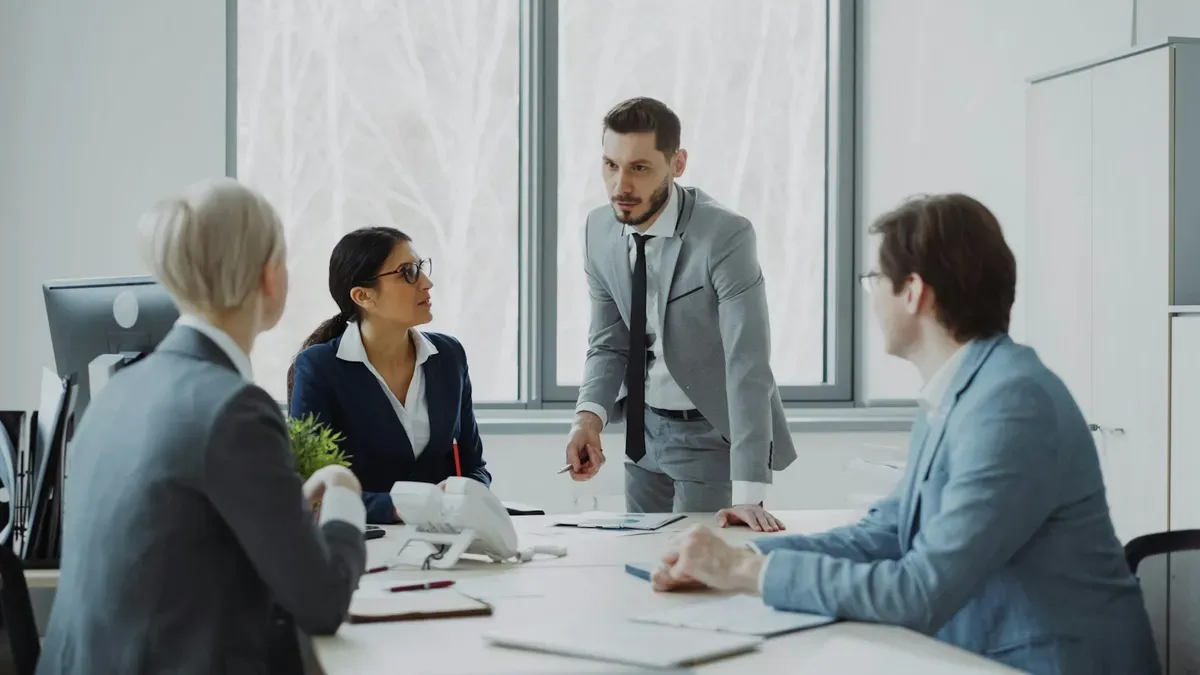 A man standing at a conference table leading a meeting with three colleagues