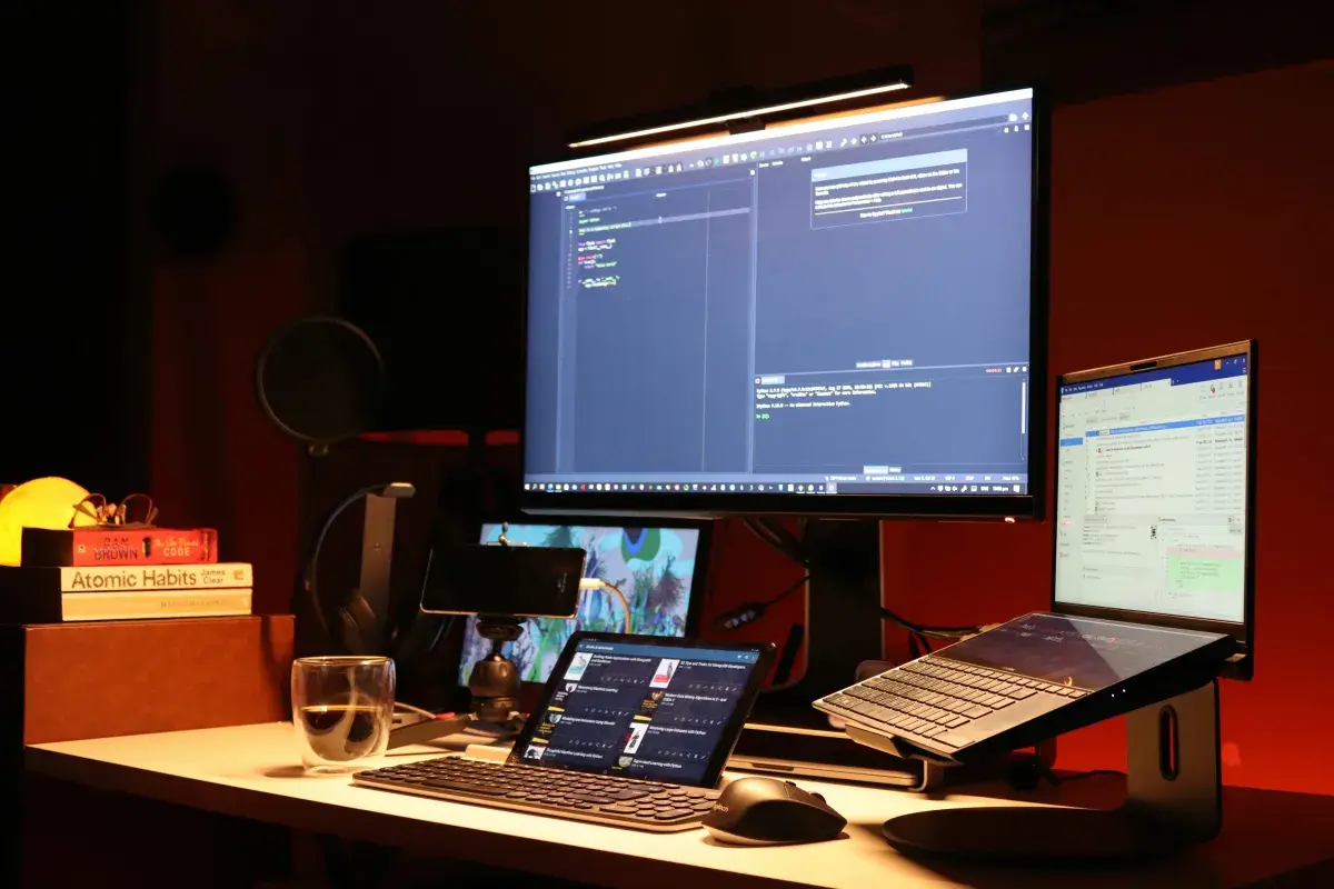Multi-monitor workstation with a code editor, terminal, and reference screens in a dimly lit office